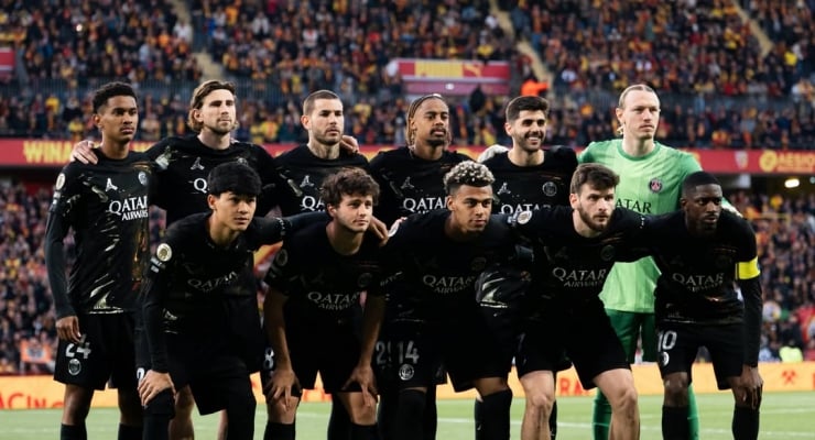 Group photo of Paris Saint-Germain players in black away kits posing with arms around each other on a football pitch, crowd in the stands behind them.