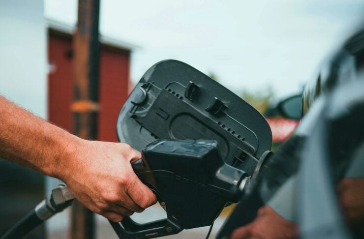 Person hands holding a gas pump nozzle and refueling a car at a station, the nozzle near the fuel door on a dark vehicle