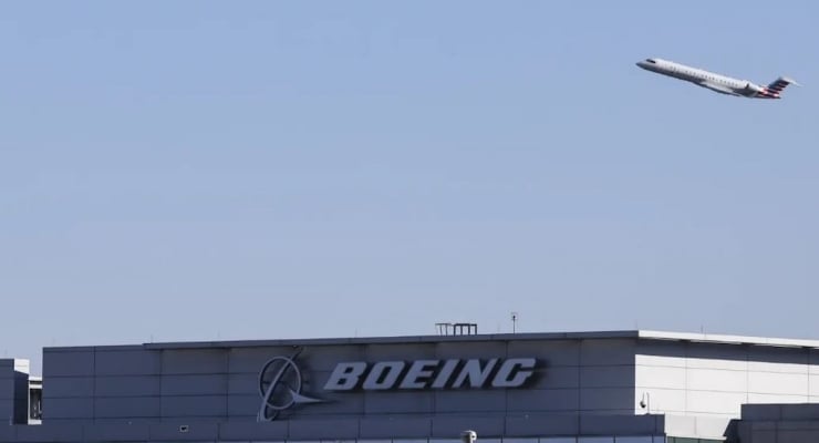 Airplane taking off above the Boeing building against a clear blue sky.