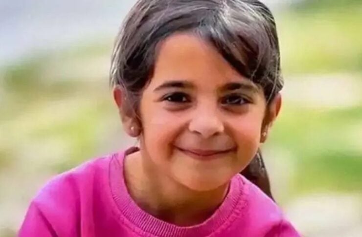 Smiling young girl with dark hair in a pink sweater outdoors in a park.