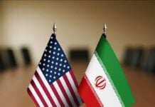 Two small national flags, United States and Iran, stand on a conference table, symbolizing diplomacy and dialogue.