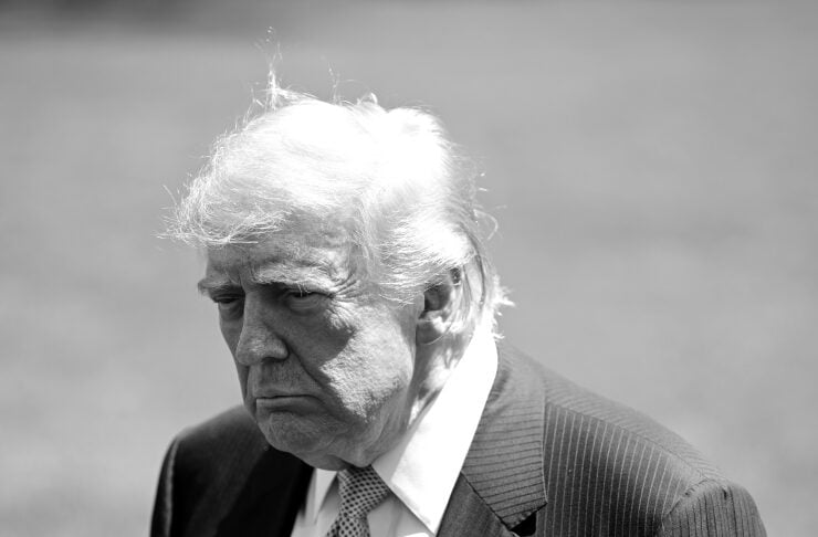 Black-and-white portrait of an older man in a pinstriped suit and light tie, looking downward with a somber expression.