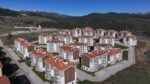 Aerial view of a new residential complex with white buildings and red-tiled roofs arranged around curved roads in a hilly landscape.