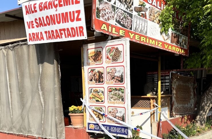Turkish restaurant storefront with red and white signs and a menu board showing kebab dishes; the entrance is taped off with blue-and-white tape and a red carpet fragment on the pavement.