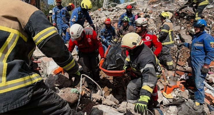 Rescue team in helmets and protective gear carries a person on a stretcher from rubble.