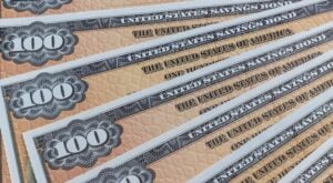 Stack of overlapping U.S. $100 bills fanned diagonally, showing the orange security design and large '100' numerals.