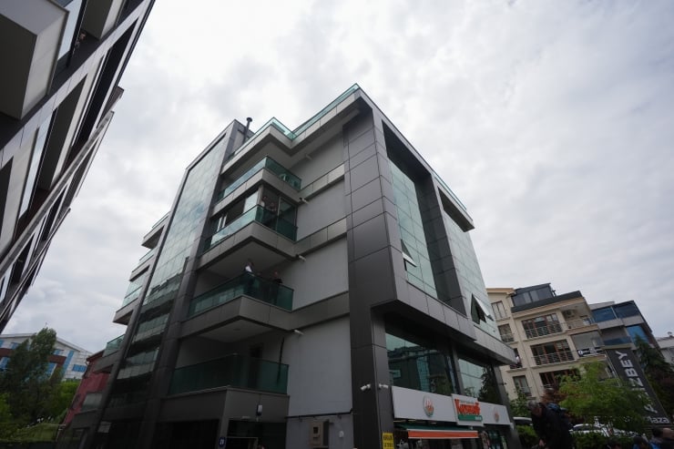 Modern glass-fronted, multi-story building with protruding balconies seen from the street under a cloudy sky.