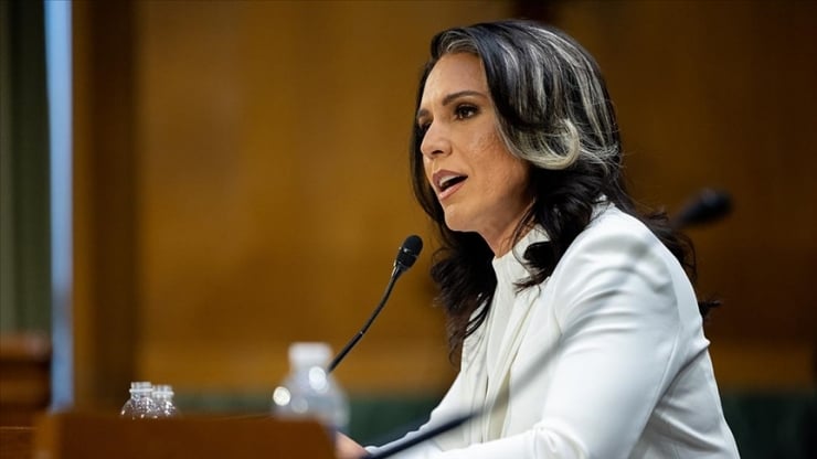 Woman in a white blazer speaks into a microphone at a podium during a formal event.