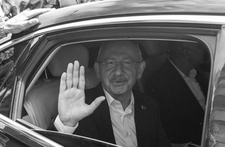 Man in a suit waves from an open car window at a crowd during a public event