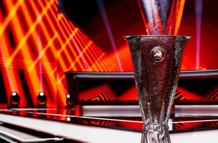 UEFA Europa League trophy on a glossy podium with red neon stage lights in the background.