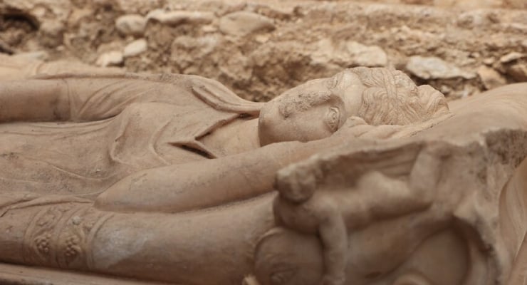 Stone statue of a reclining figure lying on its side in a dusty excavation site.