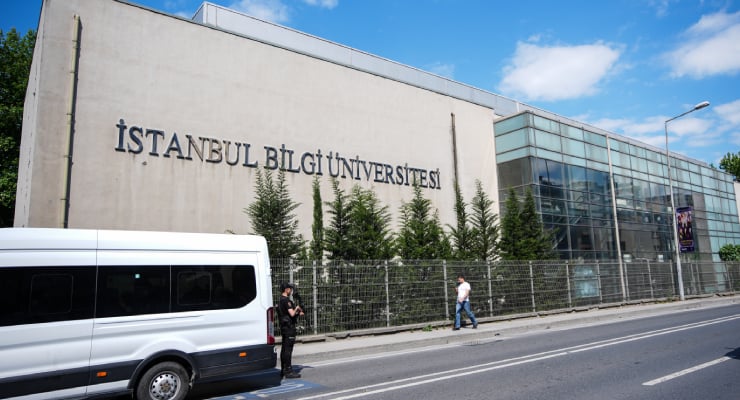 Istanbul Bilgi University campus building with a glass facade, trees, and a white van parked on the street.