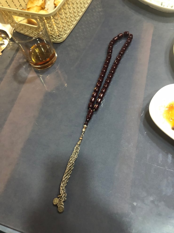 Dark wooden prayer beads with a metal tassel and coin charms, laid on a blue table surface.