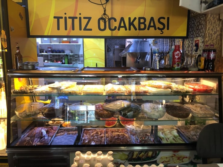 Kebab shop display case filled with grilled meats and trays of food, with a yellow sign reading 'TITIZ OCAKBAŞI' above.