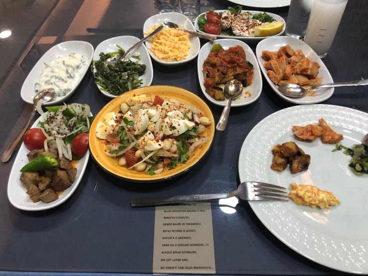 Turkish meze spread on a dark table with various bowls of salads, yogurt-dill sauce, roasted vegetables, and small plates of bites.