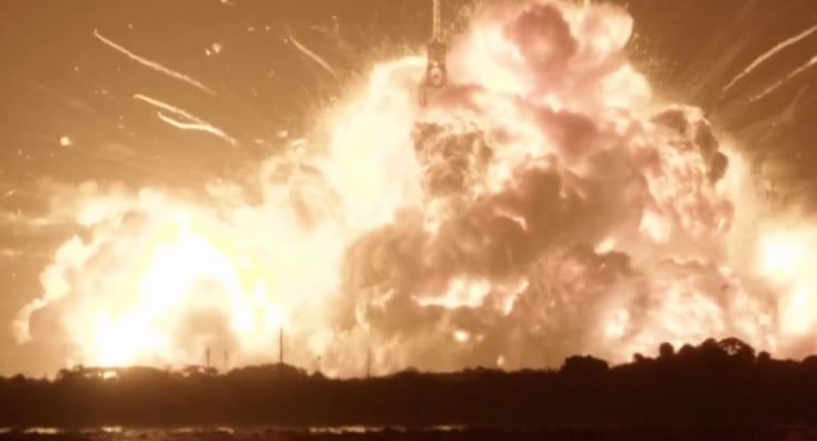 Massive explosion at night with a bright orange fireball and dark smoke expanding above a horizon.