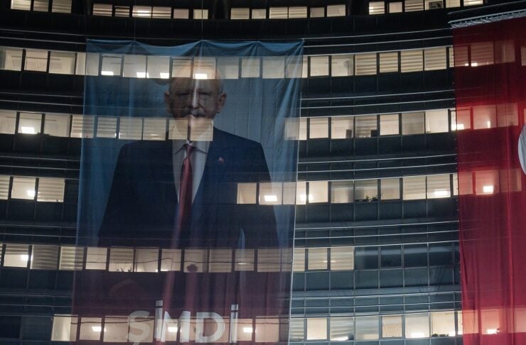 Large campaign banner hanging on a glass-front building featuring a man in a suit and bold white letters across the banner.