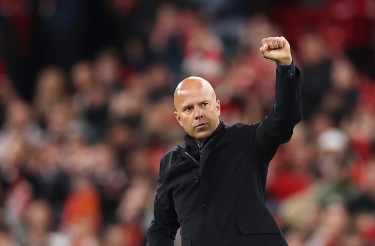 Bald man in a dark blazer celebrates on the field, raising his clenched fist as the crowd blurs in the background.