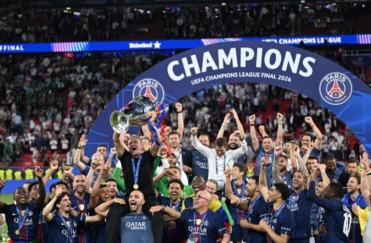 PSG players celebrate lifting the UEFA Champions League Final trophy under a 'CHAMPIONS' arch with fans cheering in the stands, 2026 final.