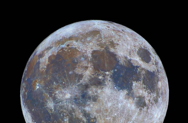 Close-up view of the Moon's textured surface with craters and maria against black space by a dark backdrop.