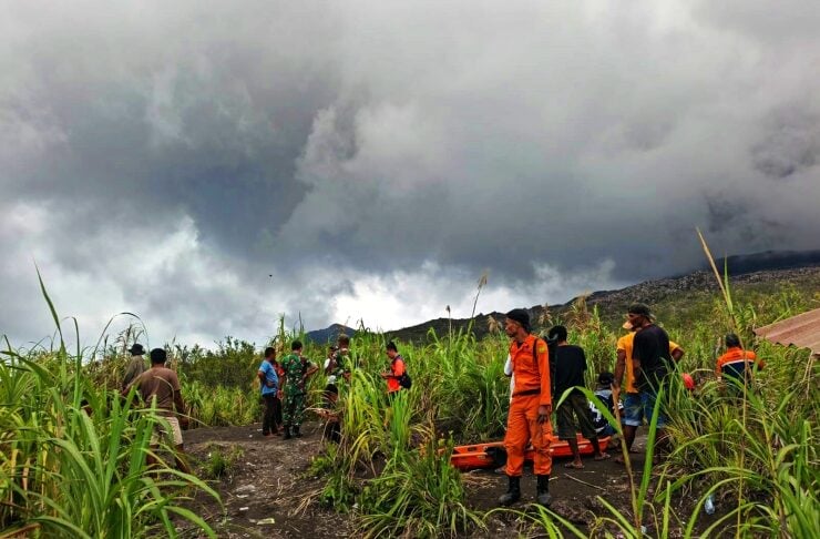 Emergency responders in orange uniforms stand in a muddy, grassy field as dark storm clouds gather overhead.