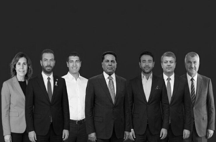 Group of seven professionals in business attire standing in a line against a dark background, looking at the camera for a corporate portrait.