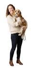 Woman wearing a beige sweater and dark jeans smiling while holding a large fluffy light-colored dog against a white background.