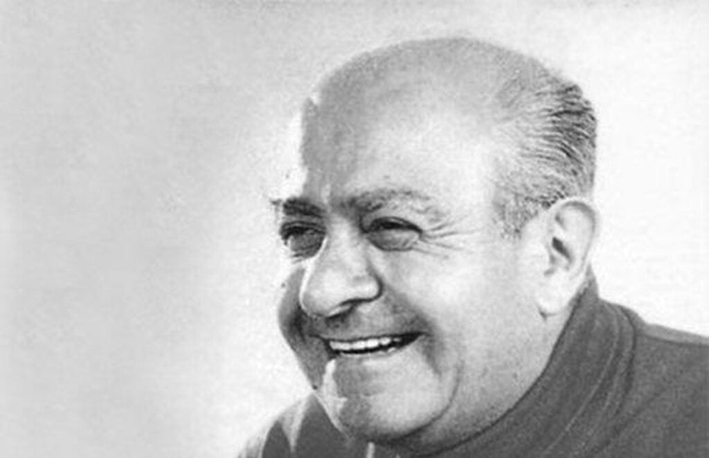 Black-and-white portrait of a smiling older man with thinning hair and a dark shirt.