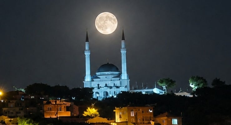 Moon rises over a white mosque with twin minarets at night, under a full moon.