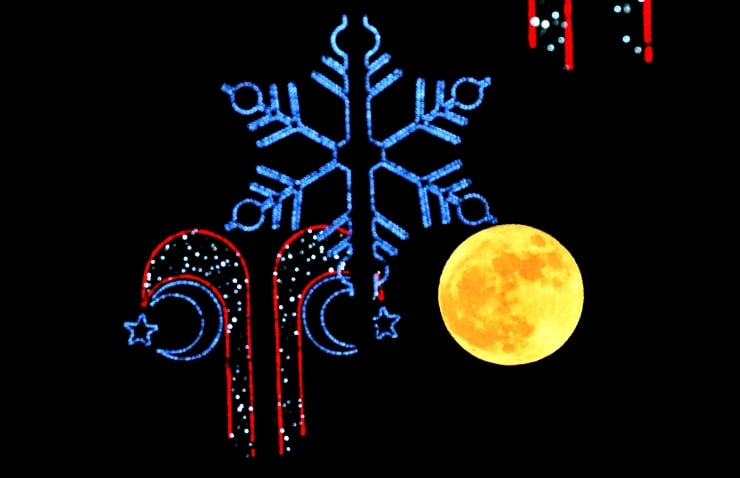 Blue illuminated snowflake with red-and-blue candy canes and a yellow full moon against a black background (holiday lights). Patchy night-sky decor.