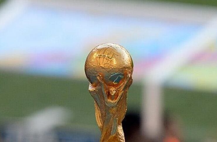 Golden World Cup trophy on a metallic pedestal with a blurred stadium background