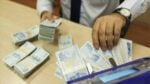 Person counting stacks of 100 Turkish lira banknotes on a table while a wristwatch is visible nearby.