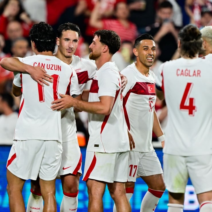 Turkish national soccer team players celebrate together on the pitch, embracing after a game.