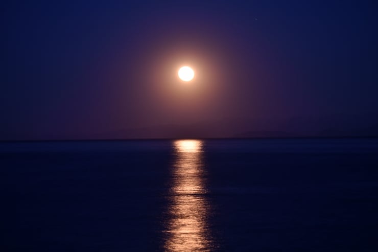 Full moon over a calm ocean at night, its reflection lighting a golden path on the water.