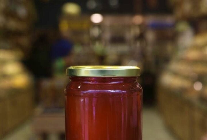 Hand holding a jar of amber jam or honey in a grocery store aisle with blurred shelves in the background.