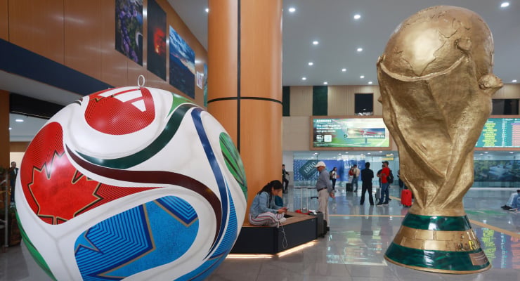 Giant World Cup trophy statue beside a oversized decorative soccer ball in a bright indoor public space.