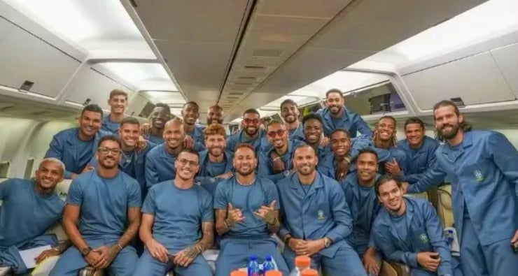 Group of men in blue uniforms posing together inside an airplane cabin, many smiling for a team photo.