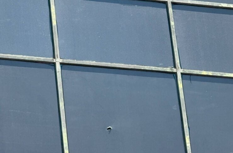 Blue glass facade with a metal grid; a small puncture/dent is visible in the center pane.