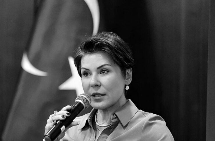 Woman seated in a panel setting, speaking into a handheld microphone during an event.