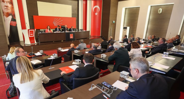 Panel of speakers at a formal conference stage in a room with Turkish flags; audience seated at desks below.