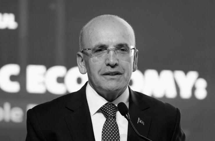 A middle-aged man in a suit speaks at a podium with a microphone at a conference backdrop.