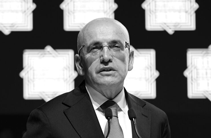 Bald man in a suit speaks at a podium with two microphones at a formal event (black and white).