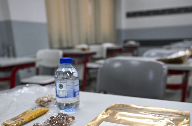 Desk setup with a blue-capped water bottle, plastic-wrapped snacks, and a large gold foil packet containing a labeled sheet.