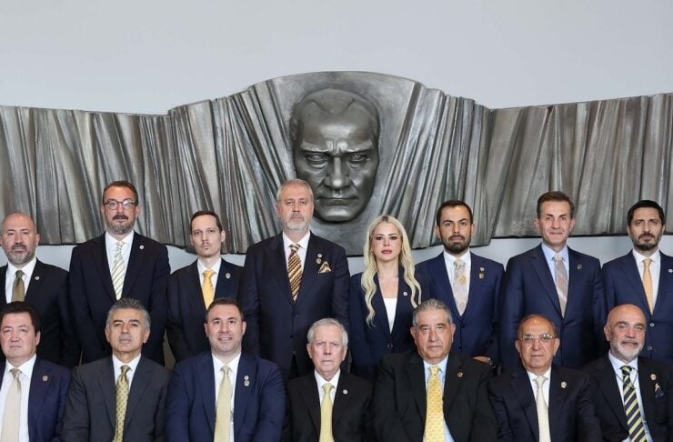 Group of formally dressed professionals posing for a portrait in front of a large sculpted head backdrop.
