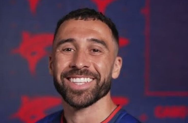 Smiling man with a beard in a blue sports jersey featuring the FCF crest, portrait against a red-blue background.