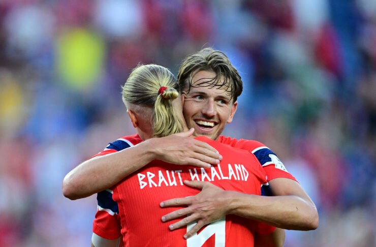 Two soccer teammates in red jerseys hug in celebration on the field, one player's back showing the number 7.