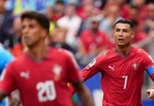 Soccer player in red Portugal kit number 7 on the field during a match, with a teammate in red nearby.