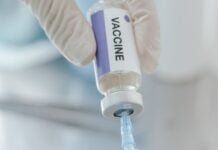 Close-up of a gloved hand drawing vaccine from a labeled vial into a syringe.