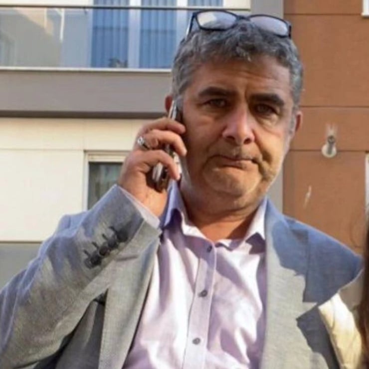 Man in a light gray blazer talking on a cell phone outdoors, wearing glasses perched on his head.