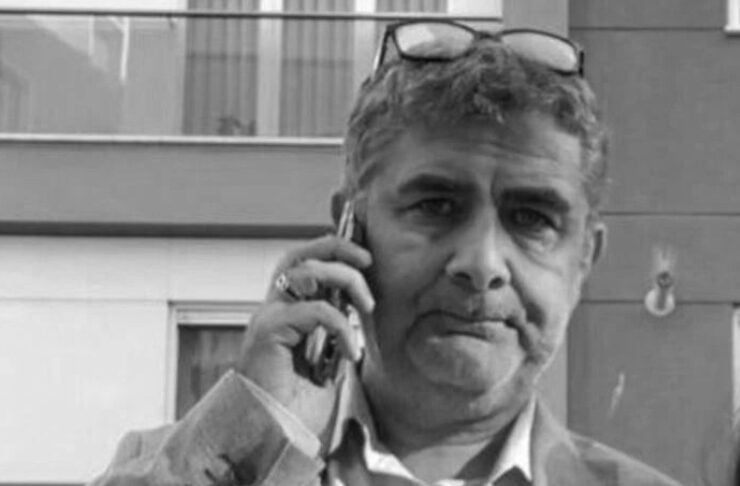 Man in a light blazer talking on a cellphone outdoors, sunglasses resting on his head.